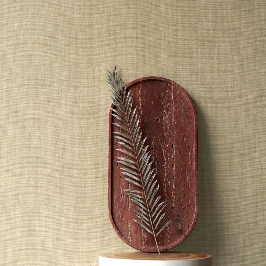 Decoratieve opstelling met een roodbruine schaal en een zilverkleurig blad tegen een beige Arte Manila Tulle 73080A behang.