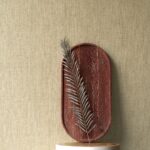 Decoratieve opstelling met een roodbruine schaal en een zilverkleurig blad tegen een beige Arte Manila Tulle 73080A behang.