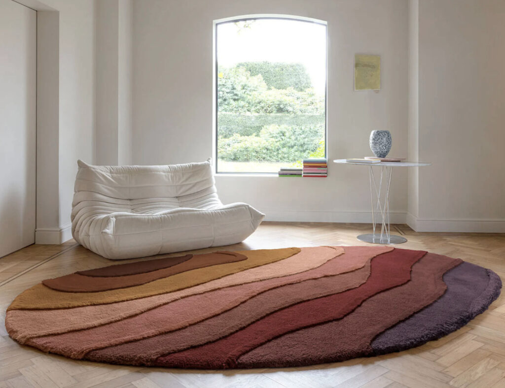 Rond Allegro High AEOH41891 vloerkleed met warme, golvende kleurbanen in een modern interieur met witte loungezetel.