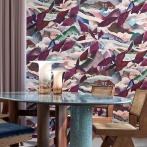Modern interieur met een ronde tafel en stoelen voor een kleurrijke Arte Alaya Manali Blueberry Hills-behangwand met abstract berglandschap.