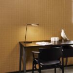 Zwarte designwerkplek met zwarte stoel, moderne bureaulamp en Arte Atelier Alma behang in mosterdgeel met subtiel rasterpatroon.