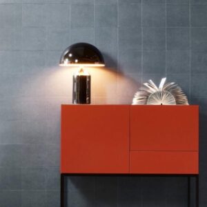 Moderne interieursetting met een rood dressoir, een designlamp en een opengevouwen boek tegen een grijs tegelmuur.