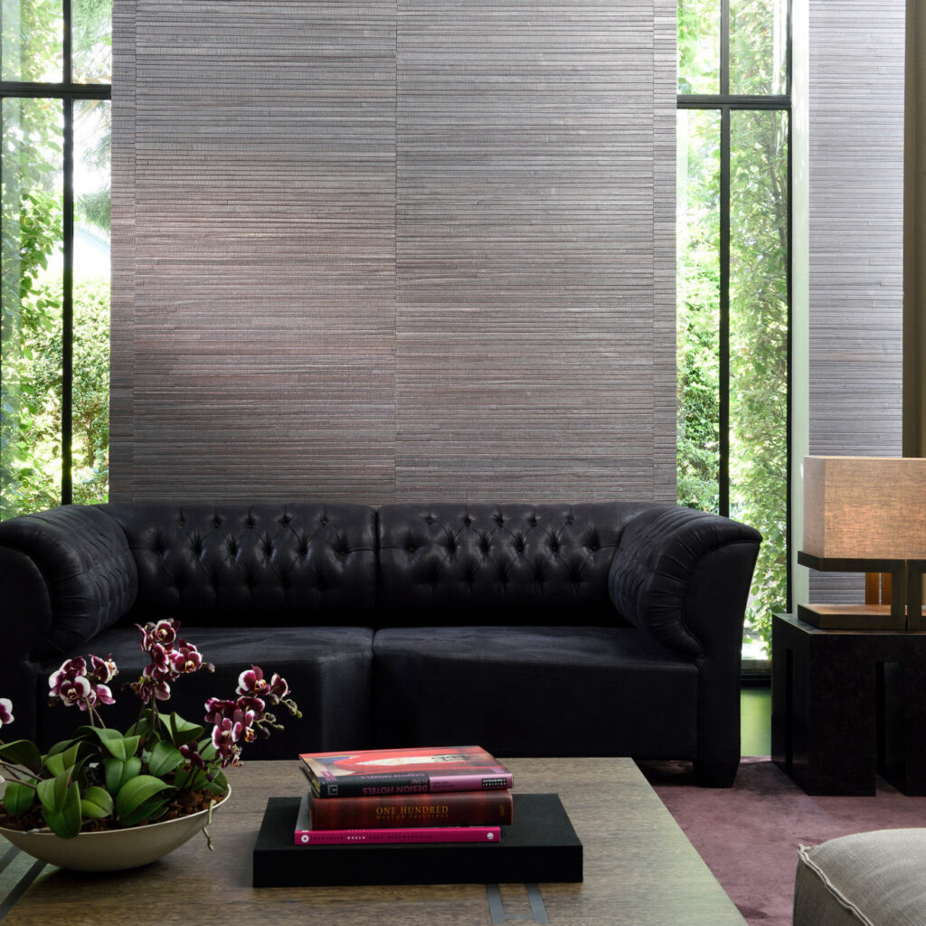 Zwarte leren bank in een moderne woonkamer met Arte Casalian 14026 behang en grote ramen met uitzicht op groen.