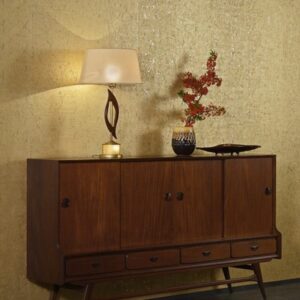 Houten dressoir met decoratieve lamp, vaas met rode takken en schaal tegen een glanzend Arte Cobra behang.