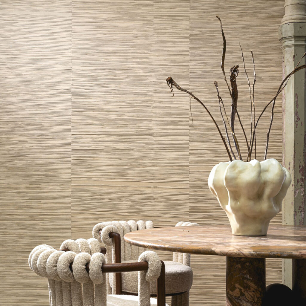 Moderne woonkamer met Arte Drift behang in zandtinten, een ronde marmeren tafel, designstoelen en een decoratieve vaas met takken.