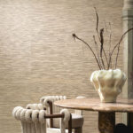 Moderne woonkamer met Arte Drift behang in zandtinten, een ronde marmeren tafel, designstoelen en een decoratieve vaas met takken.