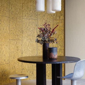 Moderne eethoek met een ronde tafel, designstoelen en goudkleurig Arte-Embleme Coti 30804-behang op de wand.