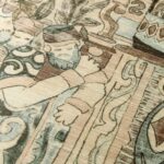 Detailopname van het Arte Emperador behang uit de Gitane collectie met een getekende figuur en decoratieve patronen in aardetinten.