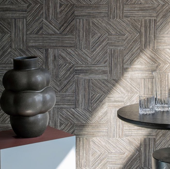 Moderne interieursetting met Arte Essentials Tangram Intarsio 24047 wandbekleding, een organisch gevormde vaas en glazen op een ronde tafel.
