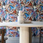 Ronde tafel met keramische vazen en borden voor een kleurrijk Arte Tangram Myriad-24102 bloemenbehang.