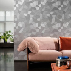 Moderne woonkamer met grijs Arte Facet behang van Buningh achter een lichtroze bank met oranje kussen.