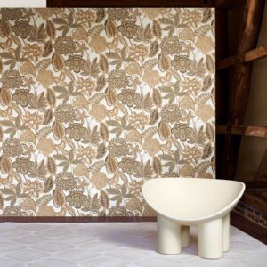 Een sfeervolle ruimte met het Arte Fiori Antichi 49560 behang uit de Gitane collectie in warme aardetinten en een modern crèmekleurig designstoel.