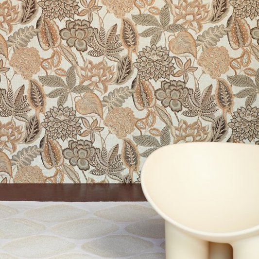 Bloemrijk Arte Fiori Antichi 49560 behang uit de Gitane collectie met warme aardetinten, naast een lichtgekleurde designstoel.