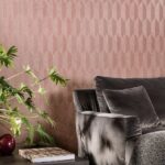 Grijze fluwelen bank met sierkussen tegen een roze geometrisch Arte Focus Symbol-26533 behang, naast een plant en bijzettafel.