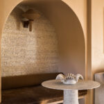 Nisvormige zithoek met Arte Fringe behang, ronde wandlamp en betonnen tafel met decoratief object.
