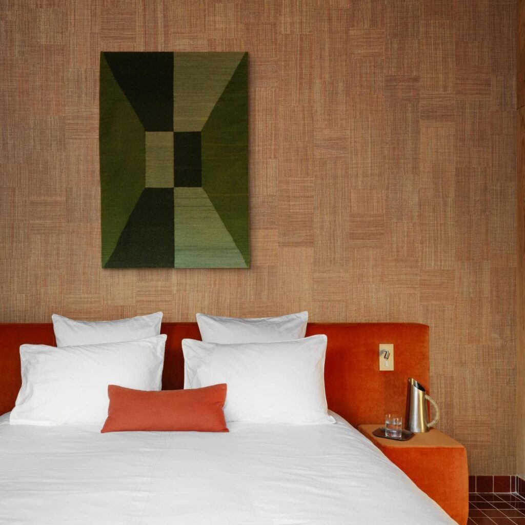 Modern ingerichte slaapkamer met een roodfluwelen bed, witte kussens, het Arte Icarus Telaio 15721 wandpaneel en een houten nachtkastje met een gouden karaf.