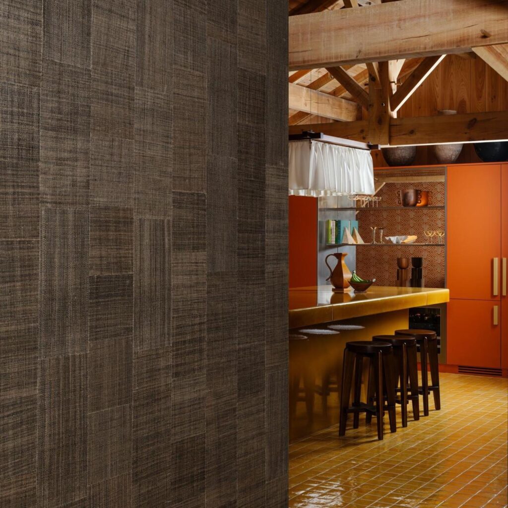 Moderne keuken met een opvallende okergele bar, oranje kasten en een muur bekleed met Arte Icarus Telaio 15729 wandbekleding in een warme, geweven textuur.
