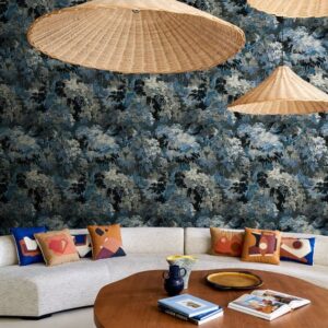 Stijlvol interieur met Arte Les Forêts Diore 48013 behang in cobalt-blauw, rotan hanglampen en kleurrijke kussens op een beige bank.