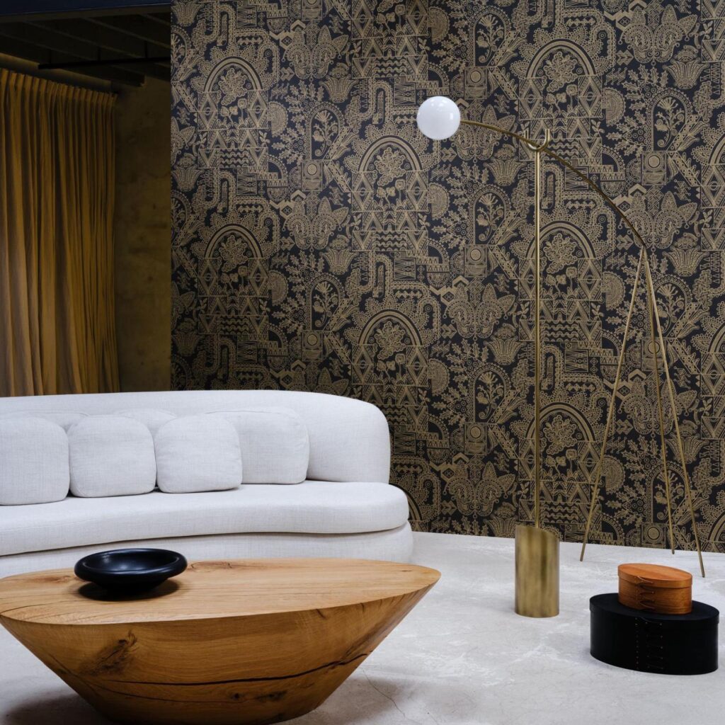Modern interieur met een lichtgrijze bank en houten tafel tegen een decoratieve zwarte muur met goud patroon van Arte Joie 30811 behang.
