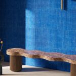 Golvend houten bankje voor een muur met blauw Arte KatanSilk 11506 behang in een moderne interieursetting.