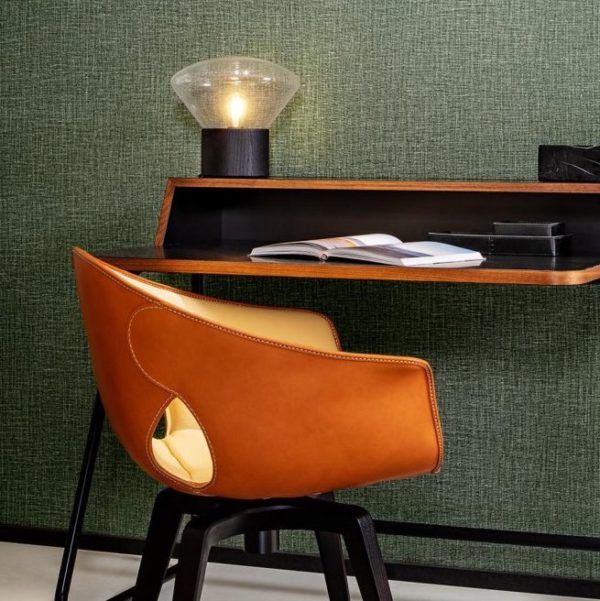 Designbureau met een leren Gioco-stoel van Arte en een tafellamp tegen een groene linnenstructuur wandbekleding.