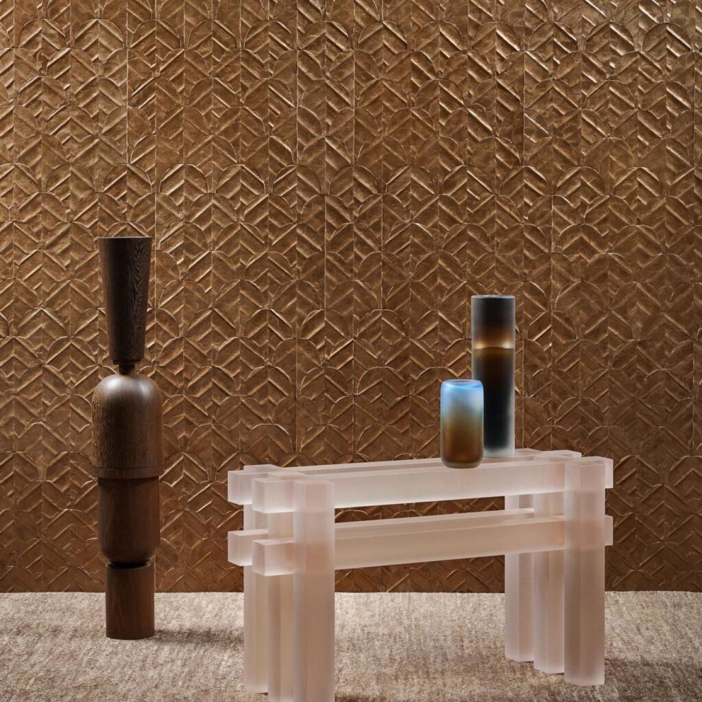 Moderne interieursetting met Arte Luster Abalone 70322 wandbekleding in koperkleur, een matglazen tafel en decoratieve vazen.