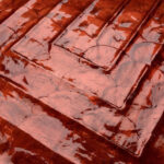Detailopname van de rode glanzende textuur van de Arte Luster Cornice 70333 wandbekleding met een geometrisch reliëfpatroon.