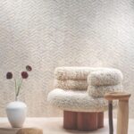 Sfeervolle interieurhoek met een Arte Luster Lucea 70310 wandbekleding, een wollige designstoel en een witte vaas met bloemen.