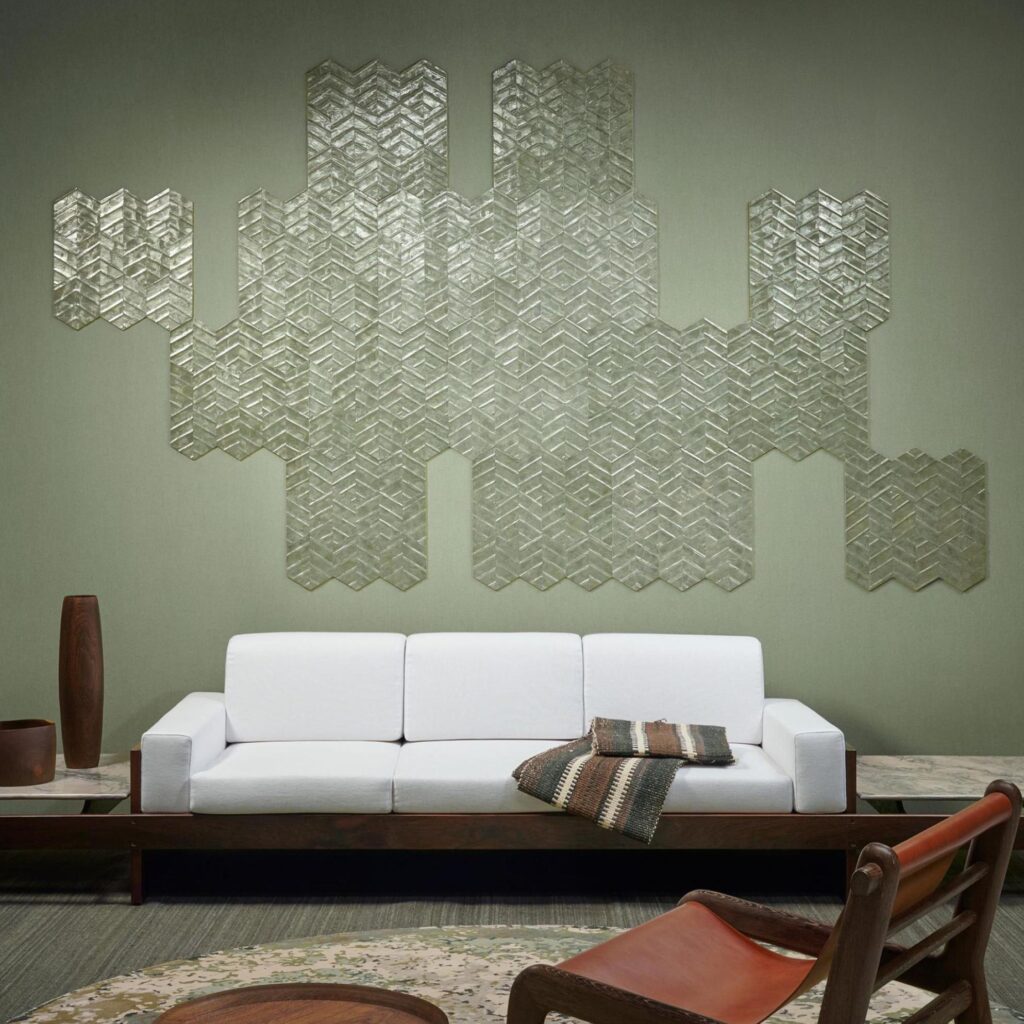 Een moderne woonkamer met een witte bank, decoratieve kussens en een wand bekleed met Arte Luster Lucea 70312 wandpanelen in een geometrisch patroon.