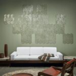Een moderne woonkamer met een witte bank, decoratieve kussens en een wand bekleed met Arte Luster Lucea 70312 wandpanelen in een geometrisch patroon.