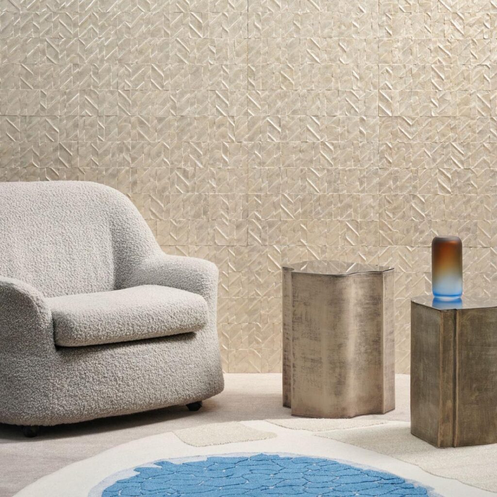 Moderne interieursetting met een zachte beige fauteuil, metalen bijzettafels en een Arte Luster Perula 70301 structuurbehang op de achtergrond.