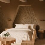 Sfeervolle slaapkamer met een Arte Marquesa Cyperus 31734-motief op de achterwand en neutraal gekleurde, moderne meubels.