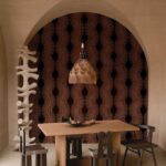 Interieur met een Arte Marquesa Miro 31741 behang in donkere tinten, houten eettafel, designstoelen en een decoratieve hanglamp.