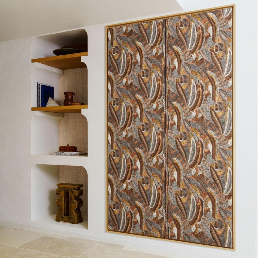 In een modern interieur hangt het wandpaneel Arte Melaky Mandrava 40761 met een organisch bruin en okergeel patroon naast een ingebouwde witte wandkast met houten planken.