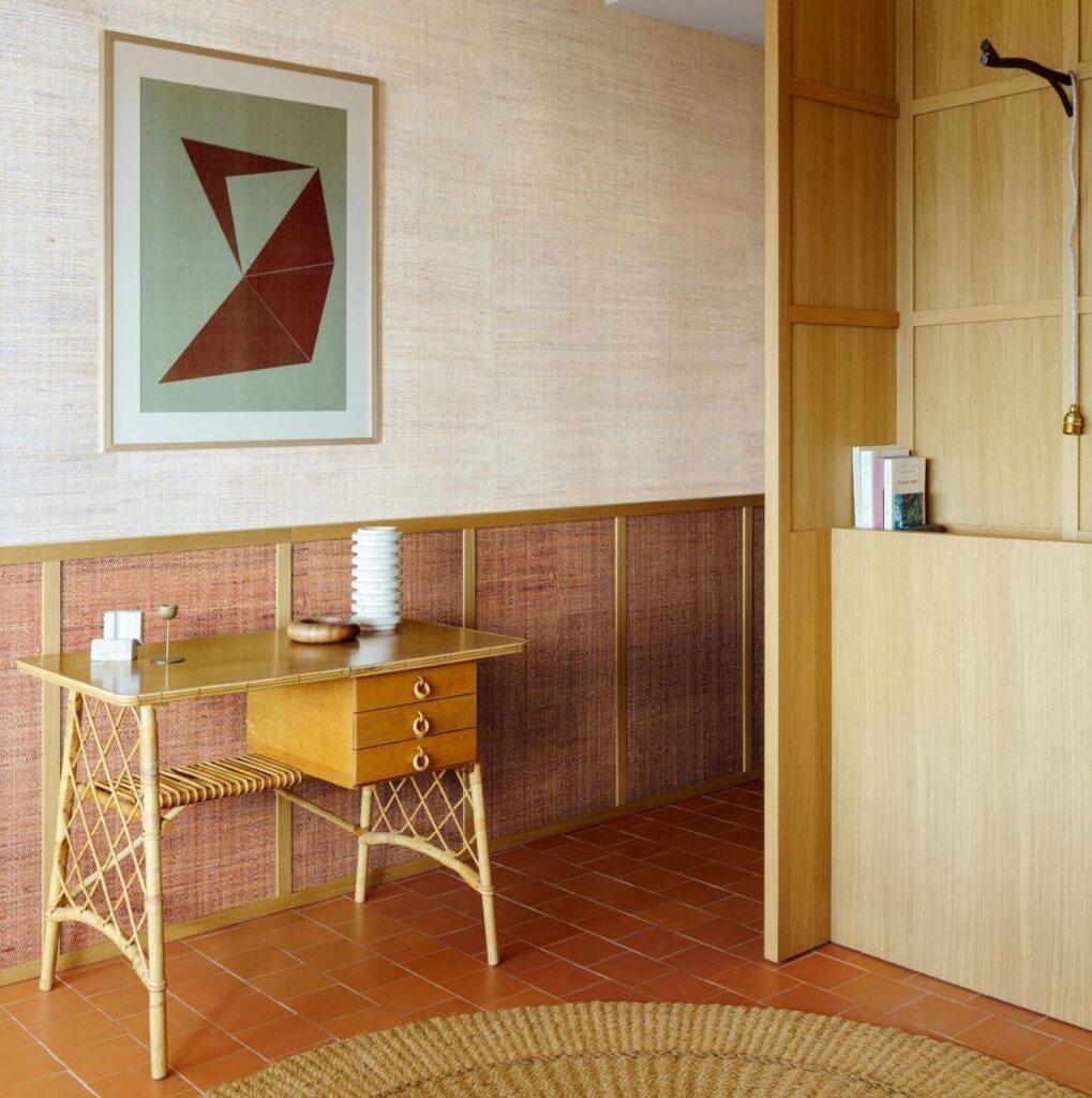 Rieten bureautje in een hal met Arte Melaky behang in warme aardetinten en abstracte kunst aan de muur.