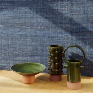 Groene keramieken objecten op een houten oppervlak met blauw Arte Melaky Tana 40747-behang als achtergrond.