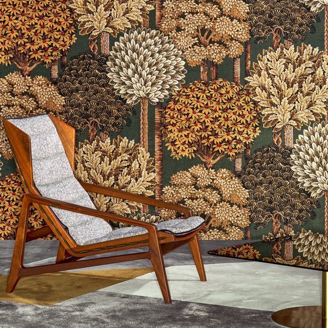 Houten loungestoel met grijze bekleding voor een wand met kleurrijk boompatroon uit de Arte MontRoyal behangcollectie.