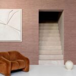 Interieur met Arte Pampas Sombra 73547 behang, een beige trap, een roestbruine designstoel, witte vaas en abstract kunstwerk aan de muur.