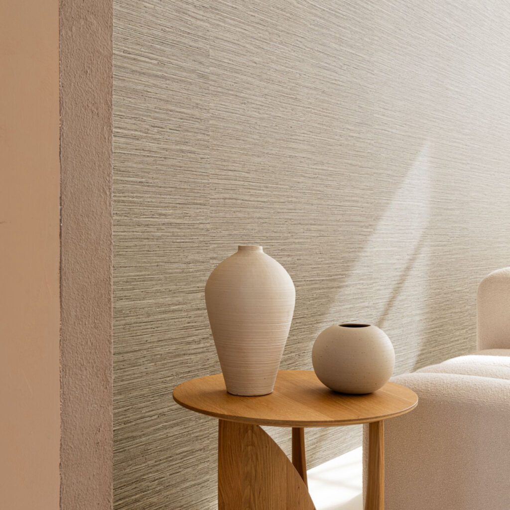 Beige Arte Pampas Matiz 73523 behang in een moderne woonkamer met houten bijzettafel en aardewerk vazen.