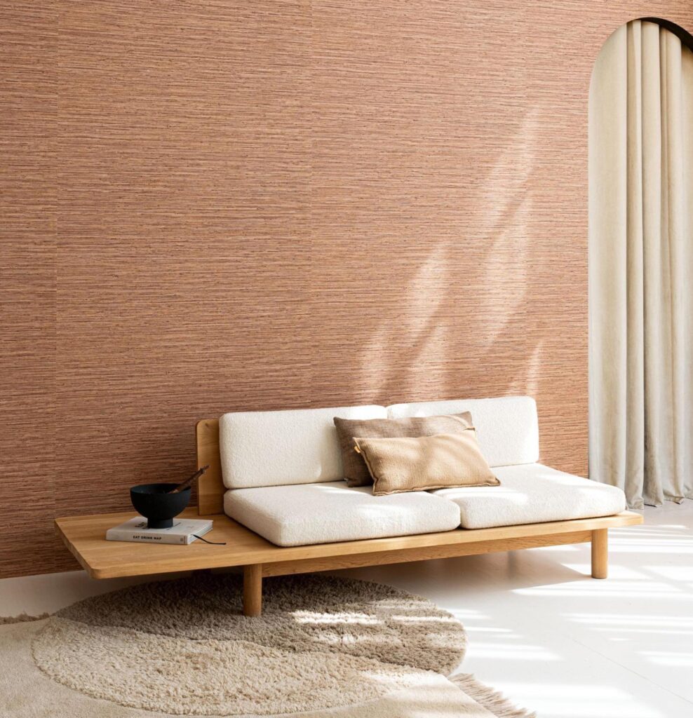 Minimalistisch ingerichte woonkamer met Arte Pampas Matiz 73526 behang in aardetint en een lage houten sofa met crèmekleurige kussens.