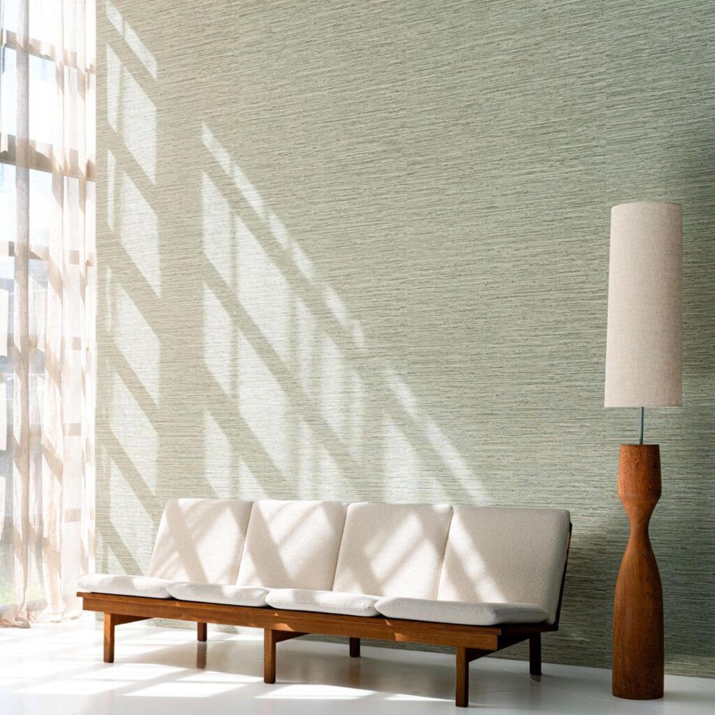 Moderne woonkamer met Arte Pampas Matiz 73532 behang, een houten bank met lichtgekleurde kussens en een bijpassende houten vloerlamp.