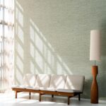 Moderne woonkamer met Arte Pampas Matiz 73532 behang, een houten bank met lichtgekleurde kussens en een bijpassende houten vloerlamp.