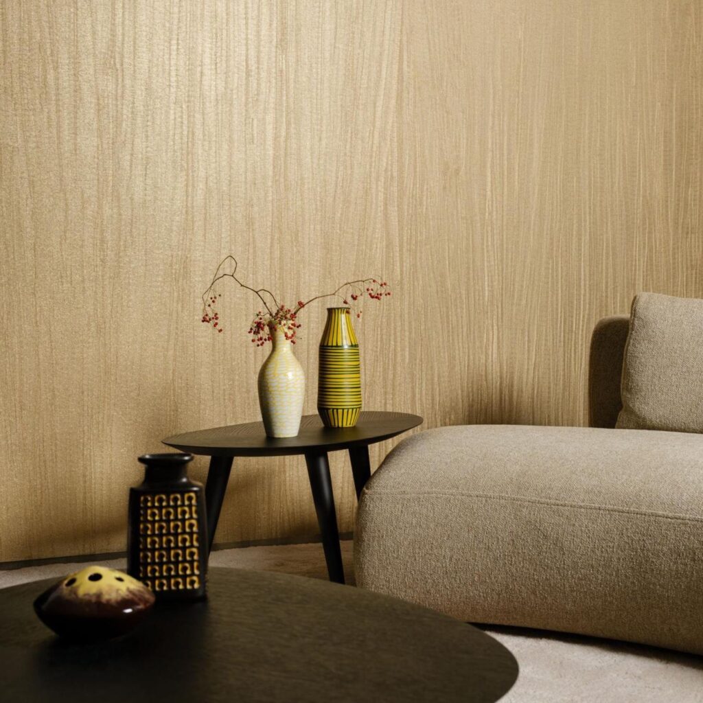 Modern interieur met Arte Pristine 23525A-behang, een beige wandbekleding met subtiele textuur, achter een beige bank en decoratieve vazen op zwarte bijzettafeltjes.