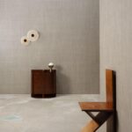 Minimalistisch interieur met Arte Pyxis 38008A wandbekleding, een houten kastje met lamp en een moderne houten stoel.