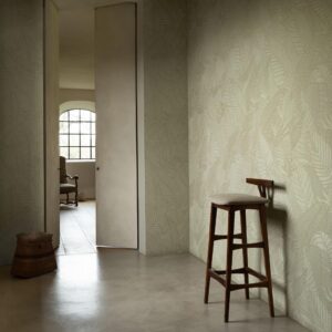 Interieur met Arte Tali Strelitzia 60740 behang, een houten kruk en zicht op een kamer met fauteuil door een open deur.