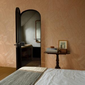 Sfeervolle slaapkamer met het bladmotief behang Arte Tali Strelitzia 60745, een open zwarte deur en een elegant bijzettafeltje met decoratieve objecten.