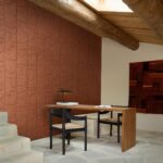 Modern interieur met Arte Terra Arcane 23914 behang in terracotta tint en houten meubelen onder een schuin houten plafond.