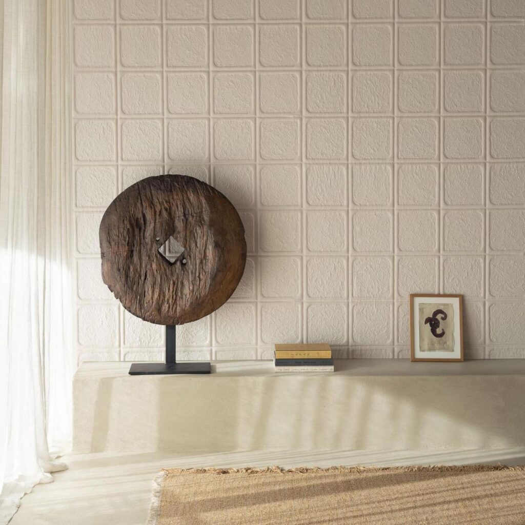 Sfeervolle interieurhoek met Arte-Terra Arcilla wandbekleding, houten sculptuur, kunstwerk en boeken op een betonnen bankje.
