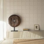 Sfeervolle interieurhoek met Arte-Terra Arcilla wandbekleding, houten sculptuur, kunstwerk en boeken op een betonnen bankje.