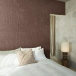 Slaapkamer met het Arte-Terra Carvato 23923-behang in aardetint met geometrisch reliëfpatroon achter een opgemaakt bed.